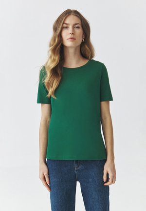 T-shirt verde a maniche corte realizzata in tessuto morbido e liscio; presenta un colletto rotondo e una vestibilità comoda, abbinato a jeans in denim blu.