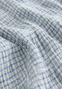 Tkanina s modro-bílým pruhovaným vzorem, s texturovaným povrchem a lehkým vzhledem, ideální pro oděvy nebo domácí textilie.