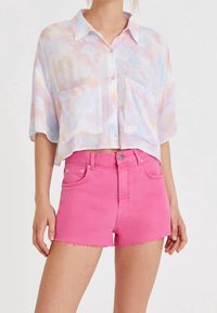 Chemise coupée aux boutons dans des couleurs pastel avec deux poches avant, associée à un short en denim rose vif avec des bords effilochés.
