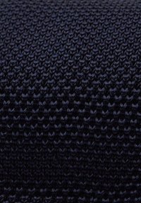 Mörk marinblå stickad textil med en enhetlig, texturerad yta och intrikata mönster av sammanflätade stygn. Mjuk och hållbar tyg.