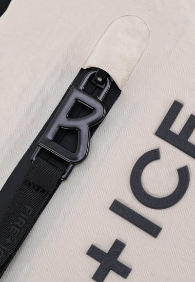 Cream fabric bag featuring a large, embossed black letter "B" and black hardware. The design includes a textured surface and sturdy strap.
