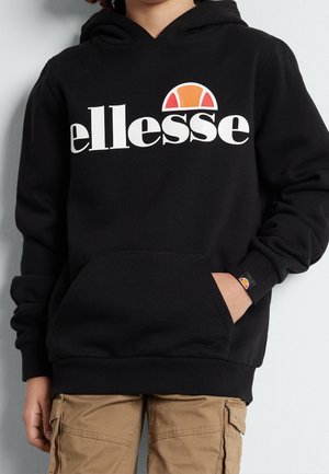 Niño con sudadera con capucha negra con gran logo blanco "ellesse" y diseño semicircular en color naranja-rojo, combinado con pantalones cargo color beige.
