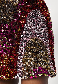 Tissu à paillettes multicolores avec une variété de paillettes brillantes rouges, roses, dorées et noires, créant une surface texturée et réfléchissante.