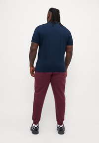 Tricou maro cu mânecă scurtă, cu guler rotund, asociat cu pantaloni de trening burgund cu croială conică și încălțăminte sport negre cu accente albe.