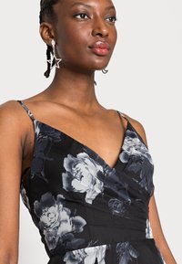 Vestido preto floral com decote em V e alças finas. Apresenta padrões de rosas cinzas e brancas, textura suave e corpete ajustado.