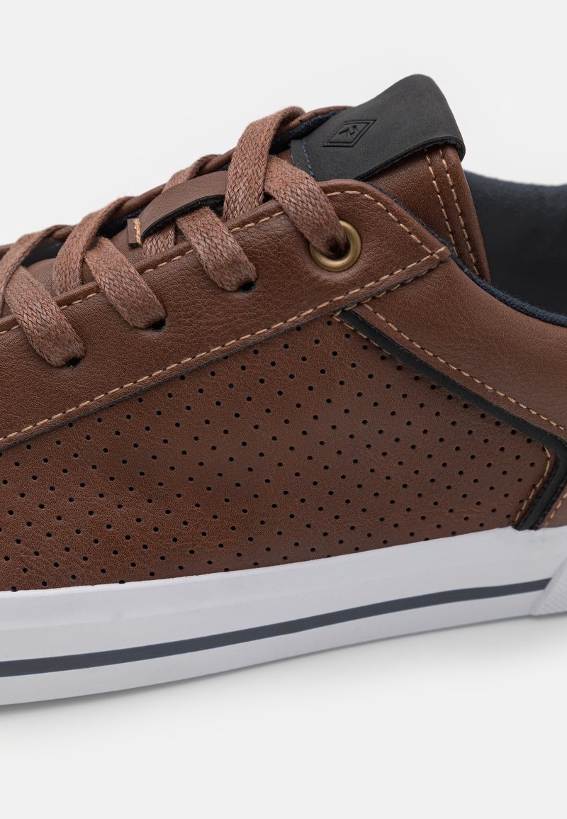 Baskets en cuir brun avec un design perforé, lacets bruns, un accent noir près de la languette, et une semelle blanche avec des rayures navy.