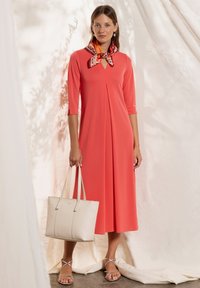 Koralfarvet kjole i knælængde med trekvartærmer og nøglehul-detalje. Sammen med en cremefarvet shoppertaske og sølvfarvede sandaler med stropper.