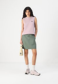Top fără mâneci de culoare mov deschis, fustă din denim verde cu buzunare frontale, geantă bej, șosete albe și adidași roz deschis. Design simplu și stil casual.
