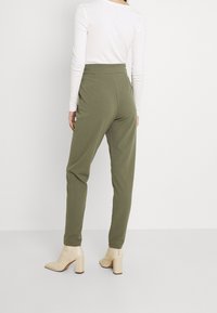 Olivgrön tapered byxor med hög midja, sidofickor och mjukt material. Bärs med beige ankellånga stövlar med en tjock klack.