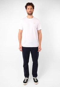 T-shirt en coton blanc avec un col rond et un petit graphique multicolore sur la poitrine, associé à un pantalon bleu marine et des baskets noires.