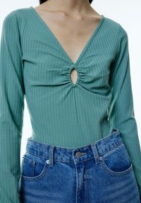Teal lange mouwen top met verticale ribbels en een keyhole-detail, gecombineerd met high-waisted blauwe denim jeans met een klassieke knoopsluiting.