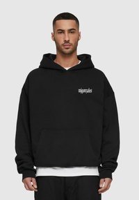 Black hoodie with a kangaroo pocket, oversized fit, and subtle white text on the chest. Made of soft fabric with a textured finish.