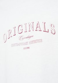 Λευκό βαμβακερό T-shirt με τυπωμένο κείμενο σε κόκκινο: "ORIGINALS Copenhagen CONTEMPORARY AESTHETICS EST.1990." Κλασικός σχεδιασμός με στρογγυλή λαιμόκοψη.