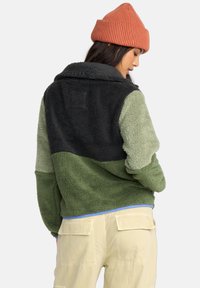 Fuzzy fleece jack in olijfgroen, groen en zwart met een kraag. Heeft een gezellig, textuur en een relaxed pasvorm. Draag het met een gebreide roestkleurige beanie.