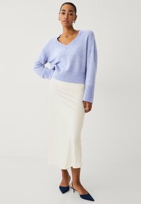 Pull v-neck lilas clair avec un ourlet côtelé, associé à une jupe midi en satin blanche. Le mannequin porte des talons aiguilles bleu marine. Texture lisse dans l'ensemble.