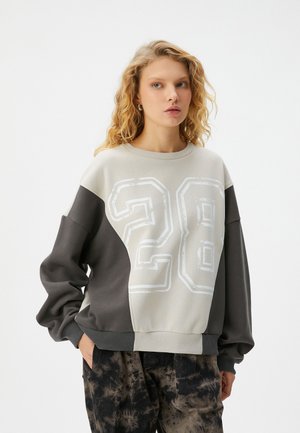 Sudadera en bloques de color gris y beige con gran impresión blanca "28". Presenta un cuello redondeado y puños acanalados, fabricada en tejido suave.