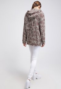 Huvtröja i dämpad olivgrön färg med ett tryck av palmblad i brunt, med långa ärmar och en avslappnad passform, matchad med vita skinnyjeans.