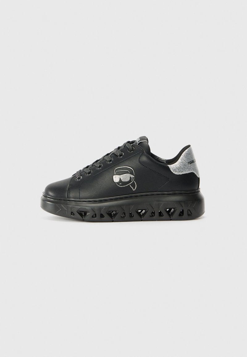 Black sneaker with a smooth leather upper, silver accent on the heel, and a chunky, textured sole featuring diamond-shaped cutouts.