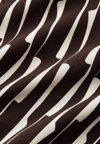 Primo piano di tessuto bianco e nero con motivo a righe ondulate, allungate e irregolari che crea un effetto fluido.