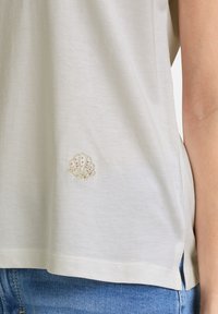 Lys beige bomulds T-shirt med dekorativ skjaldemide broderi i pastelfarver, med sidesprækker og en afslappet pasform.