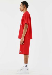 Rode T-shirt met korte mouwen en bijpassende shorts, gemaakt van een gladde stof, met logokleuren. Gekocht met witte sneakers en gestepte sokken.