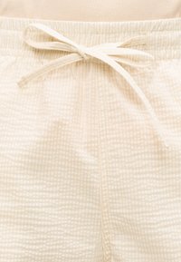 Gros plan sur une taille élastique à cordon beige à carreaux sur un pantalon ou un short en tissu léger.