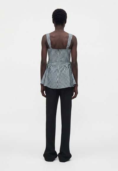 Άτομο στέκεται με την πλάτη γυρισμένη, φοράει αμάνικο μαύρο-άσπρο καρό τοπ με κλος τελείωμα και μαύρο παντελόνι ίσια γραμμή.
