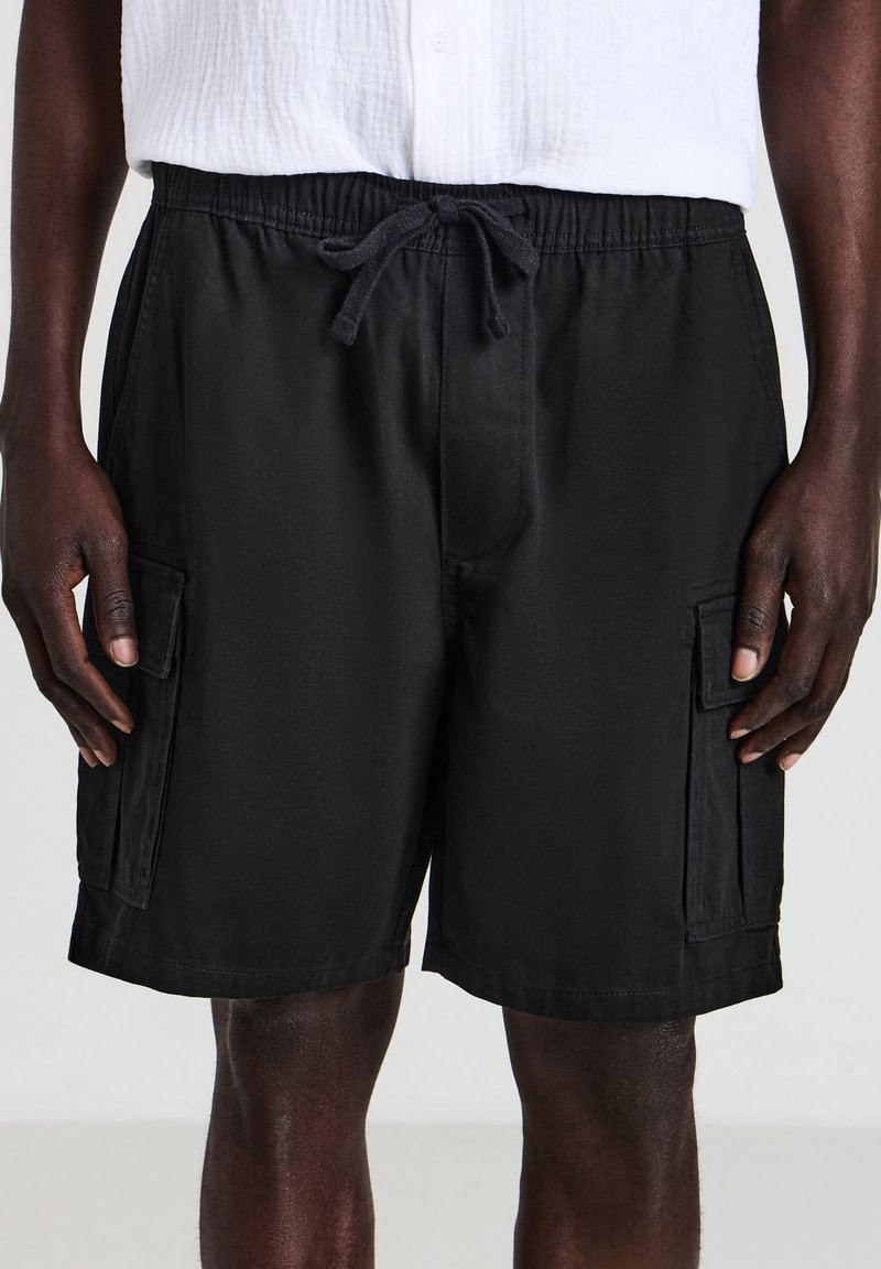 Pantaloni cargo neri con cintura elastica, lacci regolabili e due tasche laterali. Tessuto leggero con una texture liscia.