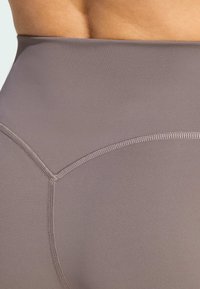 Legginsice s visokim strukom i prilagođenim krojem u prigušenoj taupe boji, izrađene od glatke tkanine s ravnim šavovima i suptilnim ukrasnim šavovima.