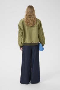 Χακί πράσινο bomber μπουφάν με υφή, σε συνδυασμό με παντελόνια φαρδιάς γραμμής από σκούρο τζιν, κρατώντας ένα ανοιχτό γαλάζιο clutch.