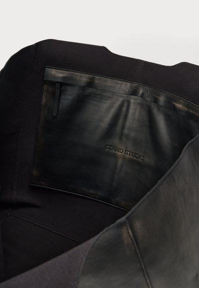 Sort lædertaske med en glat tekstur og struktureret design, der har en stor indvendig lomme mærket "STAND STUDIO."