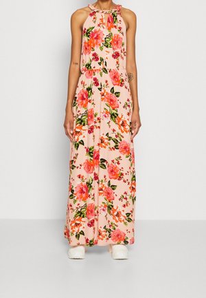 Robe maxi pêche sans manches avec imprimé floral rose vif et orange, col halter, portée avec des chaussures blanches épaisses.