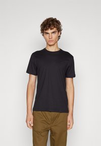 Sort kortærmet t-shirt med rund hals og diskret logodetalje. Stoffet ser glat ud og er parret med brune bukser.