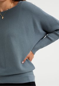 Jasnoniebieski sweter z prążkowanego dzianiny, z okrągłym dekoltem, opuszczonymi ramionami i kieszenią z przodu. Miękka tekstura i luźny krój.