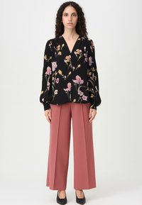 Blusa nera a fiori con fiori rosa e gialli, maniche lunghe a sbuffo e scollatura a V, abbinata a pantaloni rosa a gamba larga e scarpe nere.