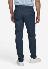 Pantalons slim-fit bleu marine en tissu texturé, deux poches arrière et fermetures à boutons contrastantes. Associés à des baskets blanches.
