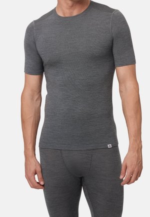 Man draagt een nauwsluitend, grijs, kort mouwen shirt en bijpassende, nauwsluitende grijze broek tegen een effen lichte achtergrond.