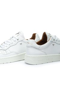 Sneakers bianchi in pelle con dettagli perforati, lacci piatti e rifiniture interne beige. Presentano il nome del brand impresso sulla parte posteriore.