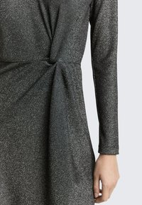 Schwarzes langärmliges Kleid aus strukturiertem Stoff mit einer Knotenapplikation an der Taille und einem subtilen Schimmereffekt im gesamten Kleid.