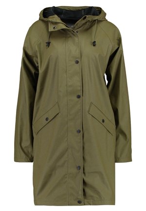 Femme portant un imperméable vert olive à boutons-pression et capuche avec cordon, d'une longueur jusqu'aux genoux, une main dans la poche, debout devant un fond blanc.