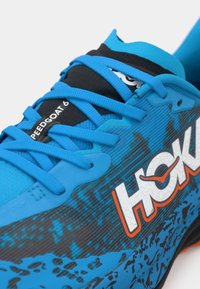 Blue athletic shoe with black accents, featuring textured upper, bold logo, and vibrant laces. Patterned design enhances visual interest.