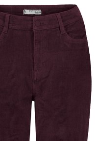 Close-up van donkerpaarse ribfluwelen broek met een voorste knoop, ritssluiting, ceintuurlussen en voorzakken, maat medium label binnenin de tailleband.