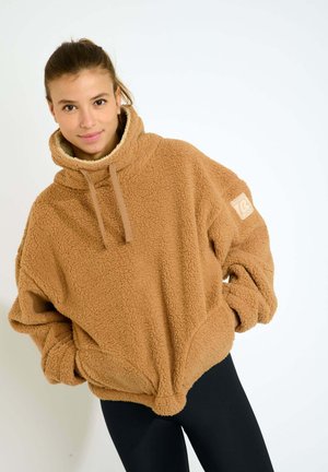Pullover in pile color sabbia con colletto alto e cordino. Caratterizzato da una morbida texture, vestibilità oversize e una toppa con logo sulla manica.
