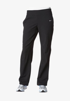Czarne spodnie sportowe Nike noszone z szaro-białymi butami do biegania na białym tle.