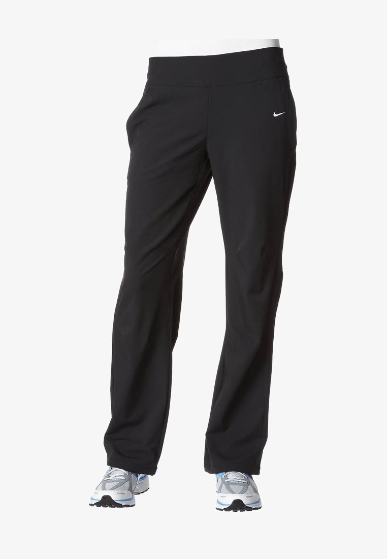 Pantalon de sport noir Nike porté avec des chaussures de course grises et blanches sur fond blanc.