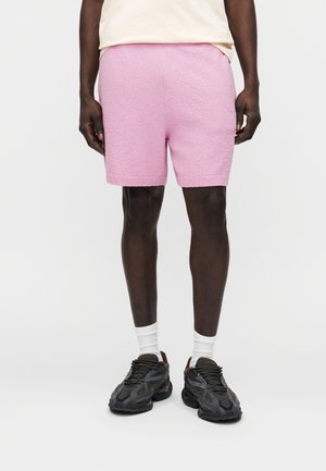Roze, gestructureerde shorts met een ontspannen pasvorm en een elastische tailleband, gecombineerd met zwarte sportschoenen en witte sokken.