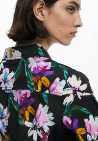Camicia nera a fiori con grandi fiori colorati in rosa, viola e giallo. Realizzata in un tessuto morbido con un design di colletto classico.