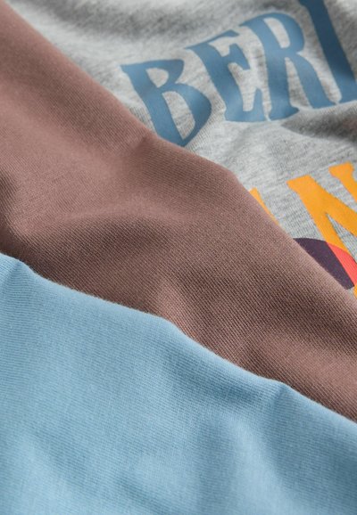 Tissu de t-shirt comprenant des sections grises, brunes et bleu clair ; présente une texture lisse avec du texte coloré et des graphismes imprimés.