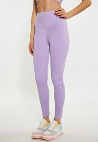 Leggings lilla realizzati in tessuto elasticizzato con vita alta, caratterizzati da una texture liscia e cuciture piatte, abbinati a sneakers chunky colorate.