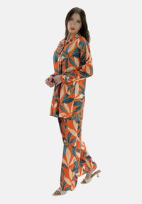 Oranje bloemenpatroon outfit met een losse shirt en broek, gemaakt van lichtgewicht stof, met groene en crèmekleurige accenten en knoopsluiting.
